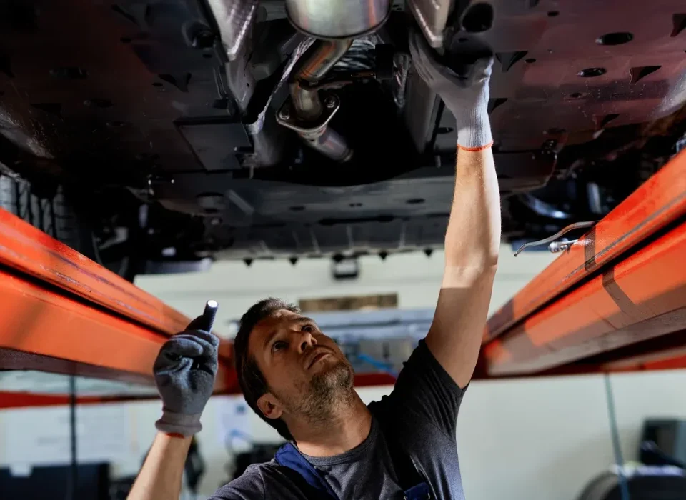 A technician inspecting the exhaust system under a vehicle at BS Services Garage in Bexleyheath.